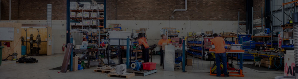 Panoramic view of the ALL-PUMPS industrial workshop and manufacturing area, featuring technicians assembling and servicing various types of large pump equipment for industrial clients
