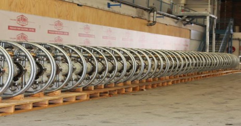 Long line of industrial pipe reels or air-operated diaphragm pump (AODD) components stored on wooden pallets in a warehouse, related to fluid transfer solutions for a coal mine