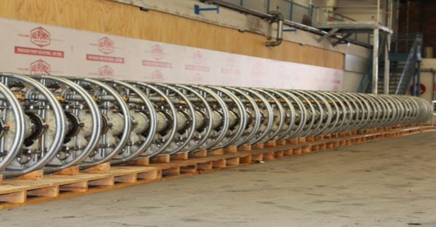 Long line of industrial pipe reels or air-operated diaphragm pump (AODD) components stored on wooden pallets in a warehouse, related to fluid transfer solutions for a coal mine