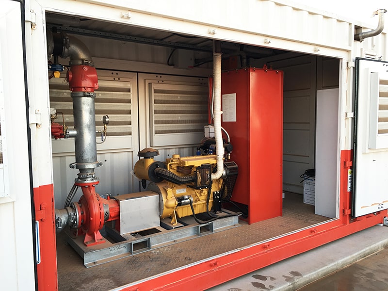 Interior of a containerized fire pump system showing the diesel-driven engine and a red centrifugal fire pump, part of a complete fire suppression package for a fuel terminal or industrial site