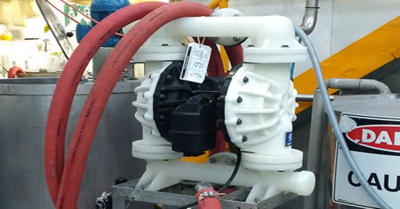 White Graco Husky 2200 plastic AODD pump connected with red industrial hoses, used for chemical transfer and fluid management in a manufacturing or chemical processing facility