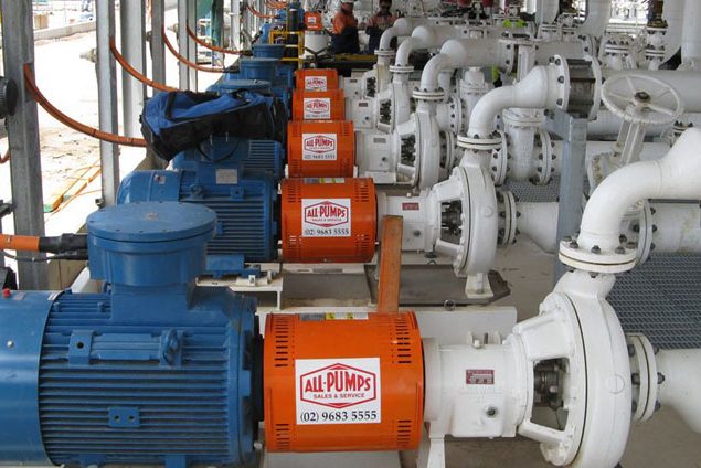 Row of white Griswold centrifugal process pumps coupled with orange and blue electric motors, installed on a concrete base at a petrochemical or industrial processing plant