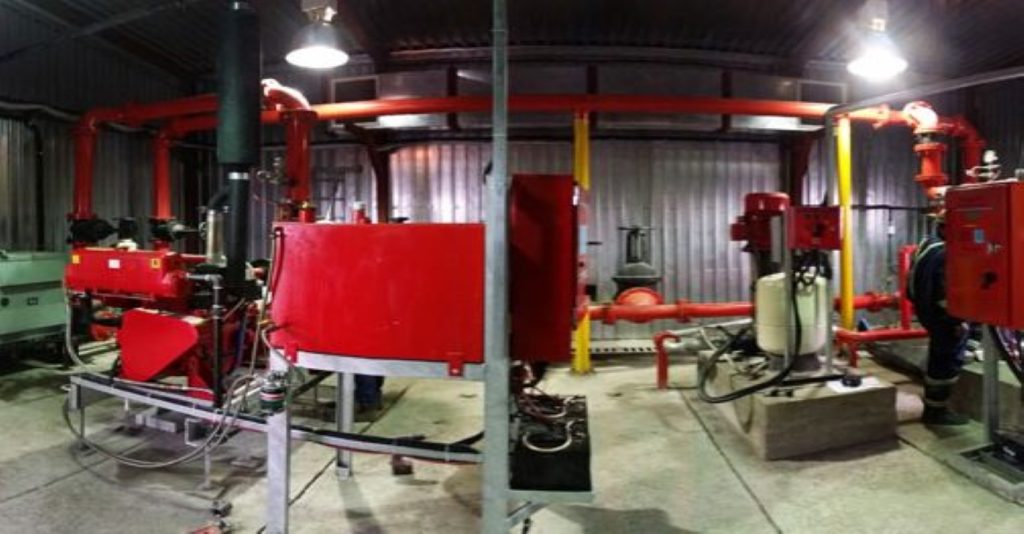 Industrial red fire suppression system installation featuring Kwikflo centrifugal pumps and red piping inside a pumphouse at the Kumtor gold mine facility