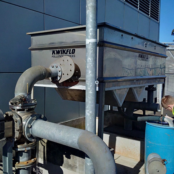 Kwikflo stainless steel oil-water separator unit installed outside a commercial building, utilizing gravity separation for wastewater treatment and compliance with environmental discharge regulations