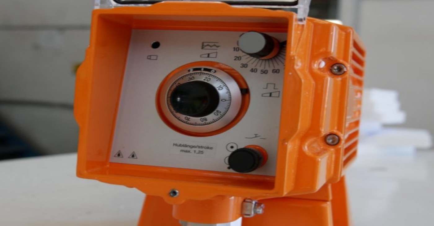 Close-up of an orange industrial metering or dosing pump control panel with a dial for setting stroke length and frequency for chemical injection or All-pumps precision fluid control