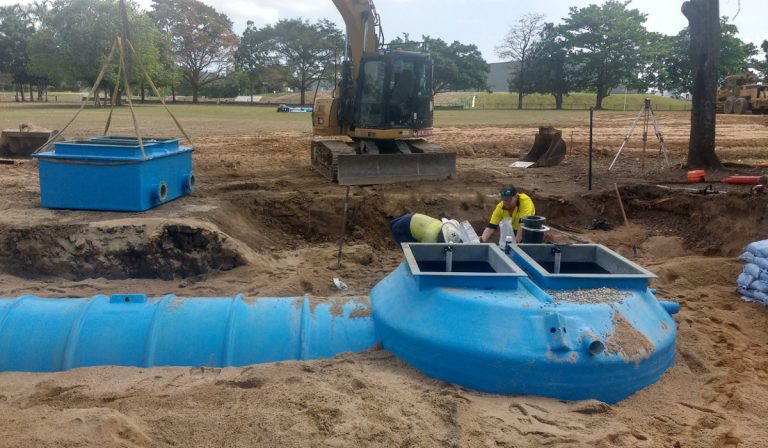 Installation of a blue packaged stormwater pump station and pre-fabricated wet well with an excavator on a civil construction site for flood mitigation and water management