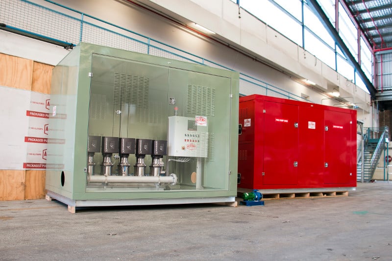 Packaged pump set and fire pump system enclosure with a green, transparent window displaying industrial-grade service water booster pumps and a red fire pump skid in a warehouse