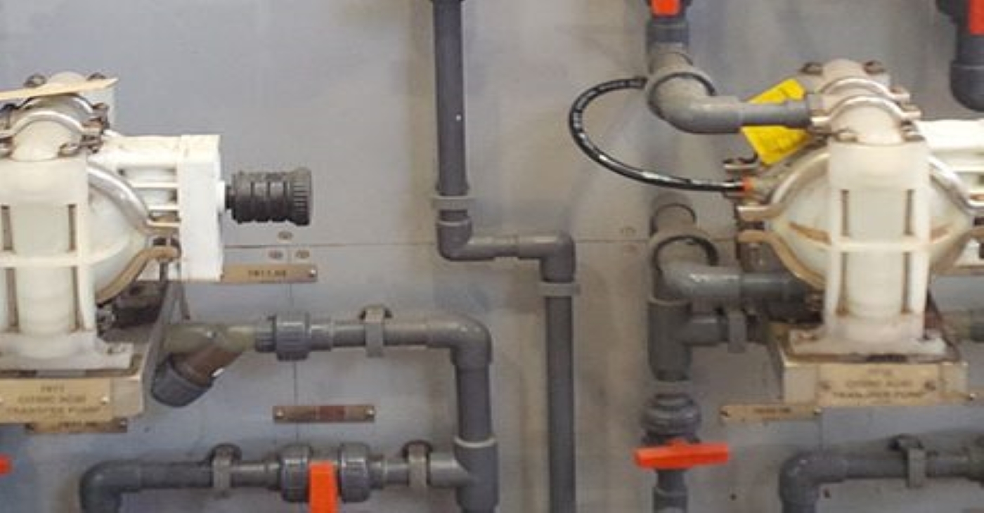 Close-up view of multiple Wilden P1 plastic AODD dosing pumps installed on a wall panel, part of a chemical injection or precise fluid control system in a process manufacturing plant