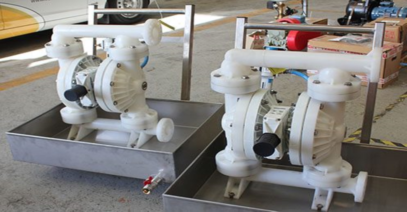Duplex installation of Wilden PX800 AODD (Air-Operated Double Diaphragm) pumps constructed from white plastic, resting in stainless steel containment trays for chemical dosing and spill prevention