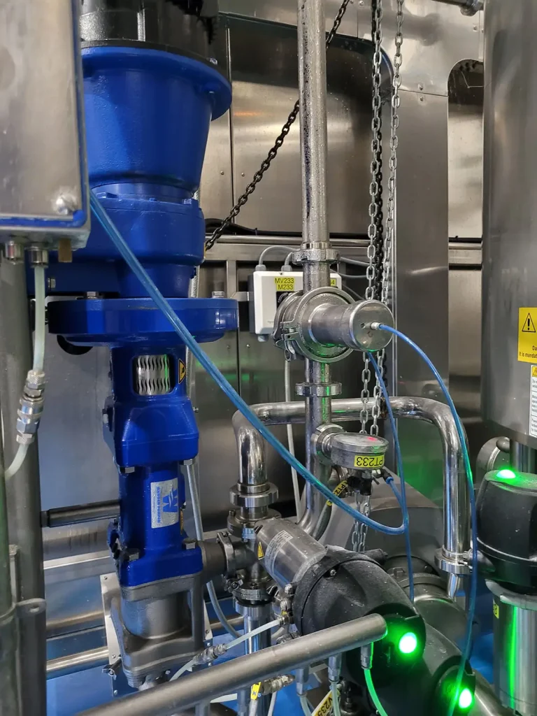 Close-up of a blue Wangen twin screw pump operating within a stainless steel processing system, used for gentle and sanitary transfer of high-viscosity products like bakery batter or food products
