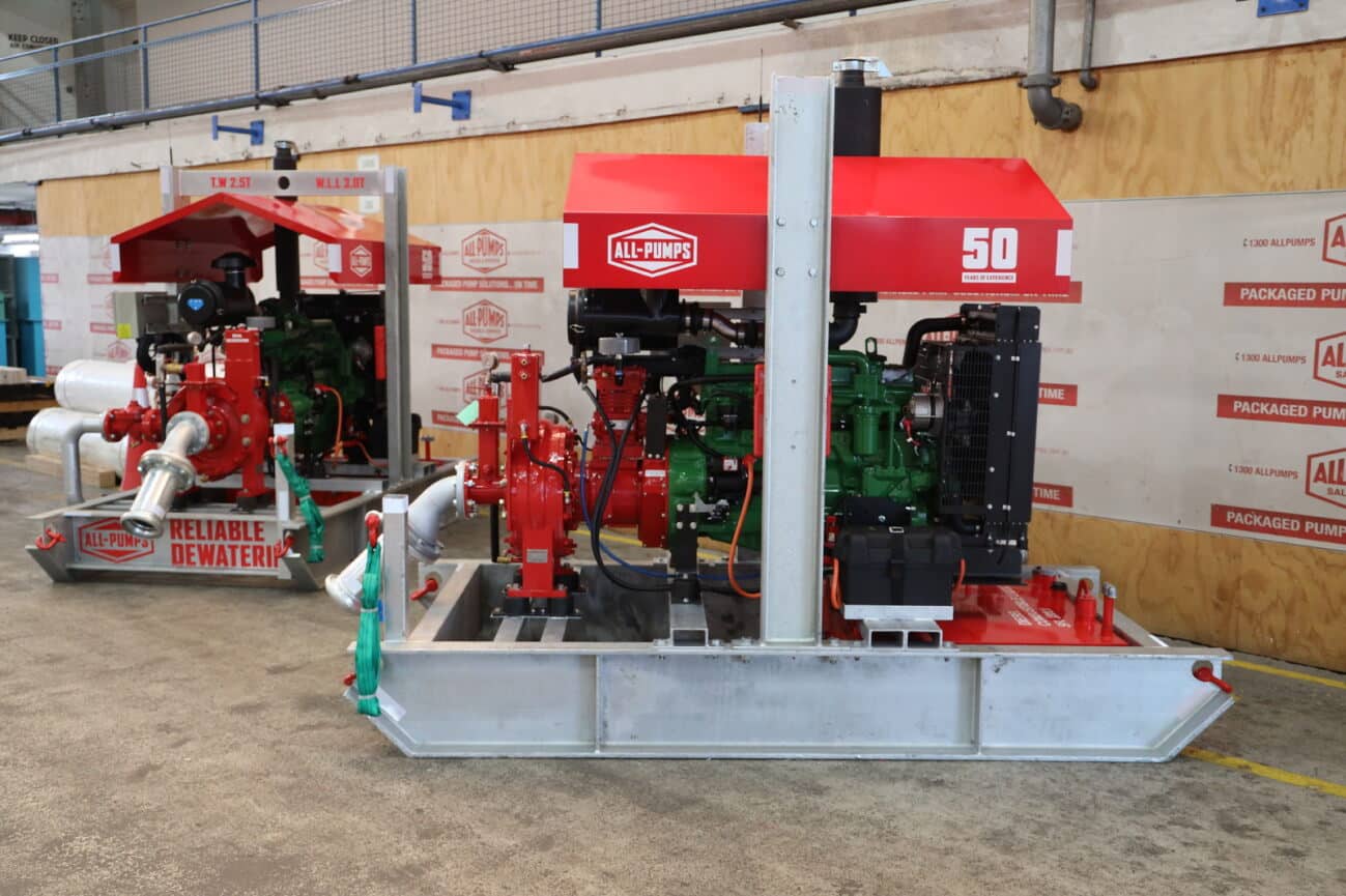 Two skid-mounted dewatering pump systems with red housings and visible All-Pumps branding are displayed inside a warehouse.