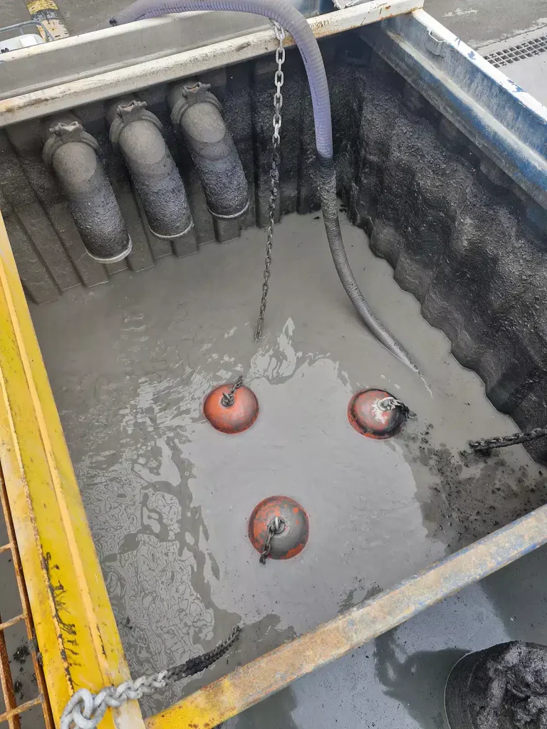 Industrial pit filled with thick sludge and oil-water mixture, showing a hose and three anchor points for an oil skimmer system used in wastewater treatment and contamination control