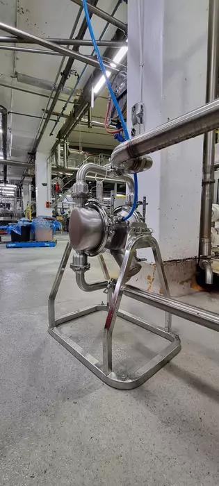 Stainless steel sanitary pump (likely an AODD or progressive cavity type) on a portable skid base, installed for hygienic transfer of meat sauce or high-viscosity food products in a food processing plant