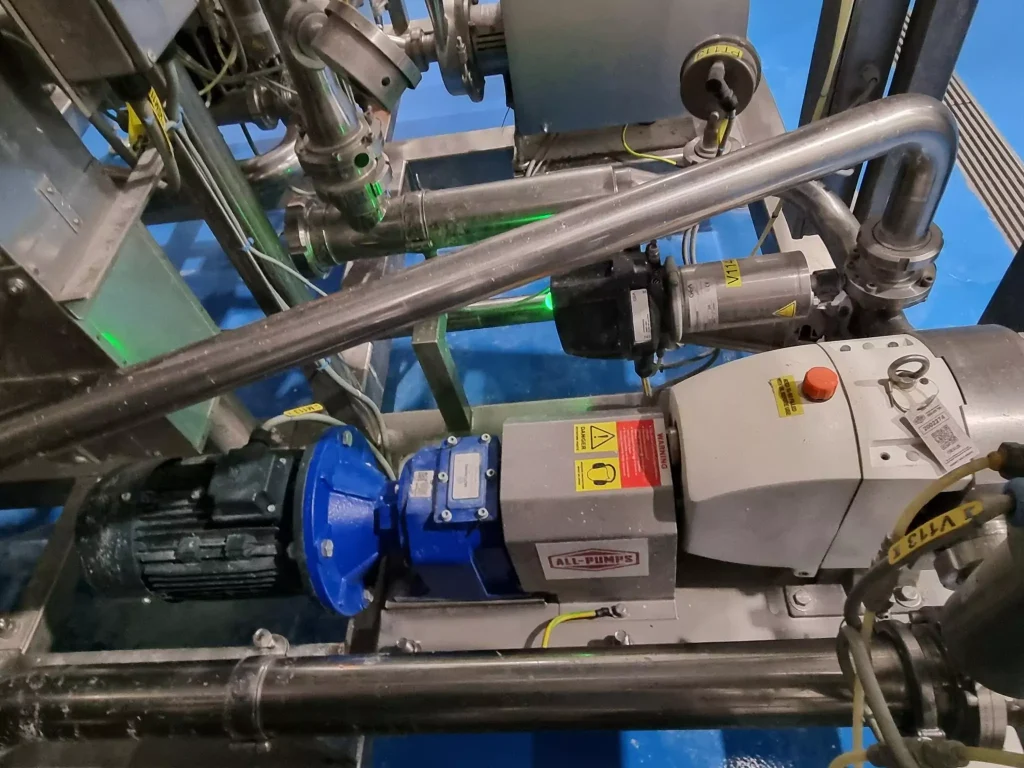 Close-up installation view of an All-Pumps supplied Jabsco lobe pump replacement unit with a blue gearbox and electric motor, used for sanitary and gentle fluid transfer in a food or pharmaceutical facility
