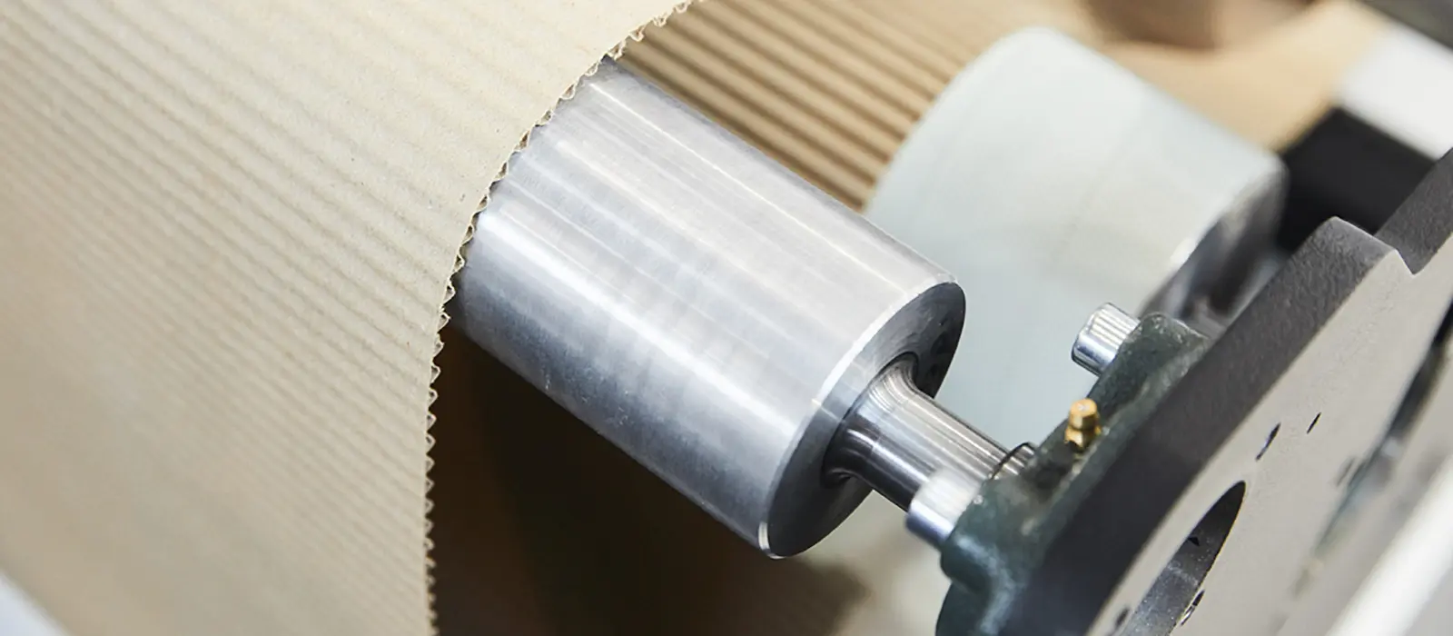 Close-up of a roller machine processing corrugated cardboard or paper board, illustrating a key process in the packaging and pulp industry requiring specialized pumps for adhesive and slurry transfer