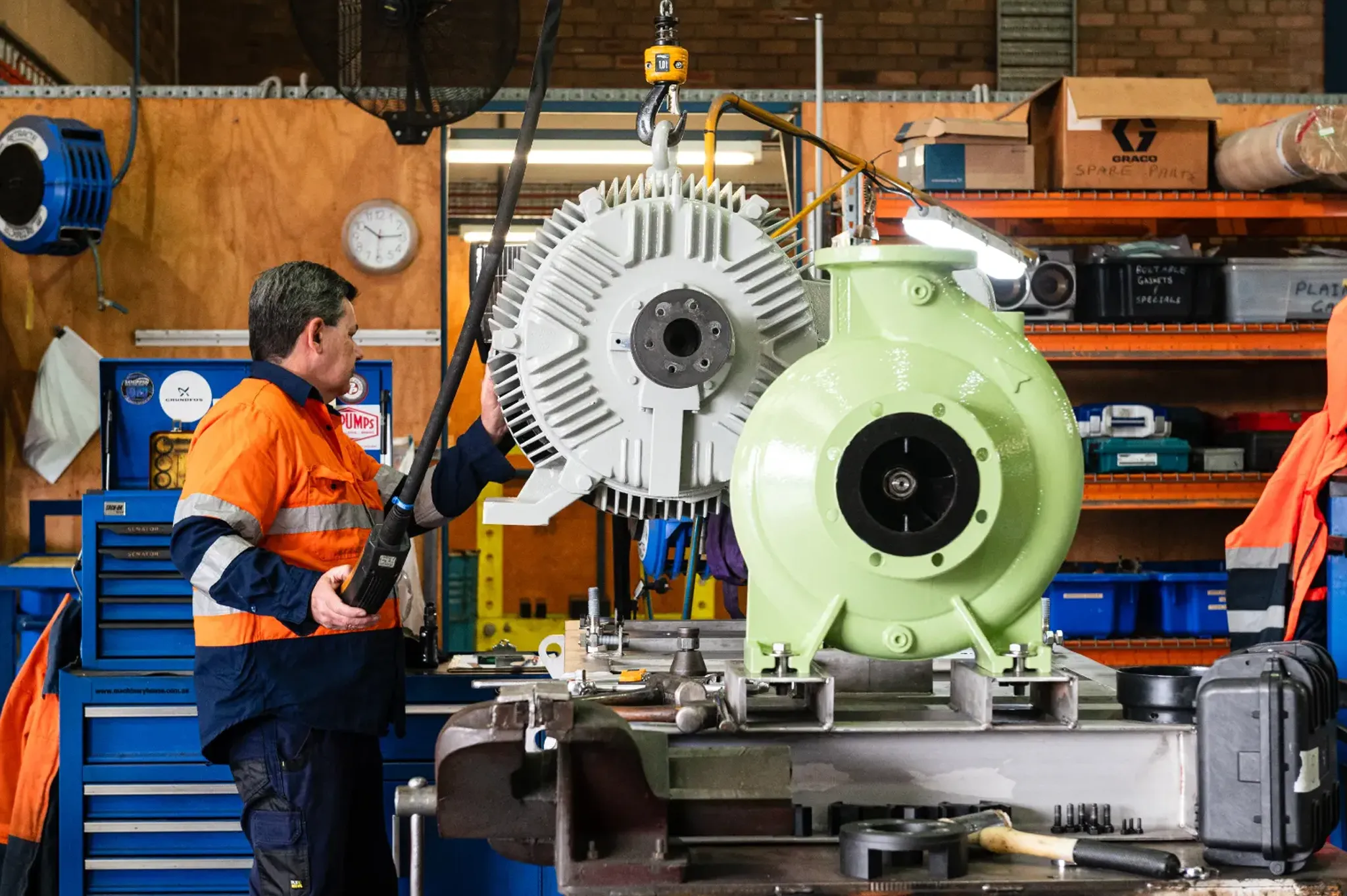 Workers beside green pump equipment in a factory